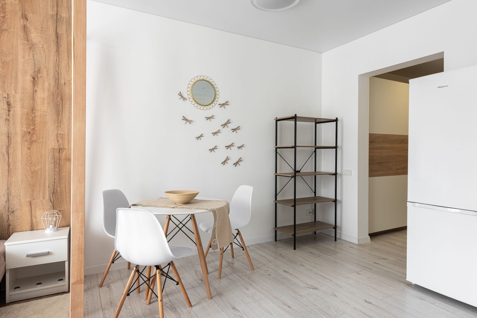 A freshly furnished open dining area in a new build, with a round table, shelving, and a wood accent wall.