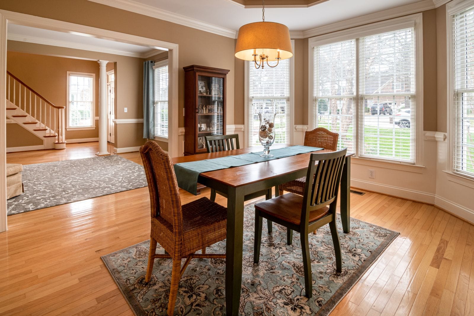 A solid-wood dining table set with chairs in a bright bay-window dining room with hardwood floors.