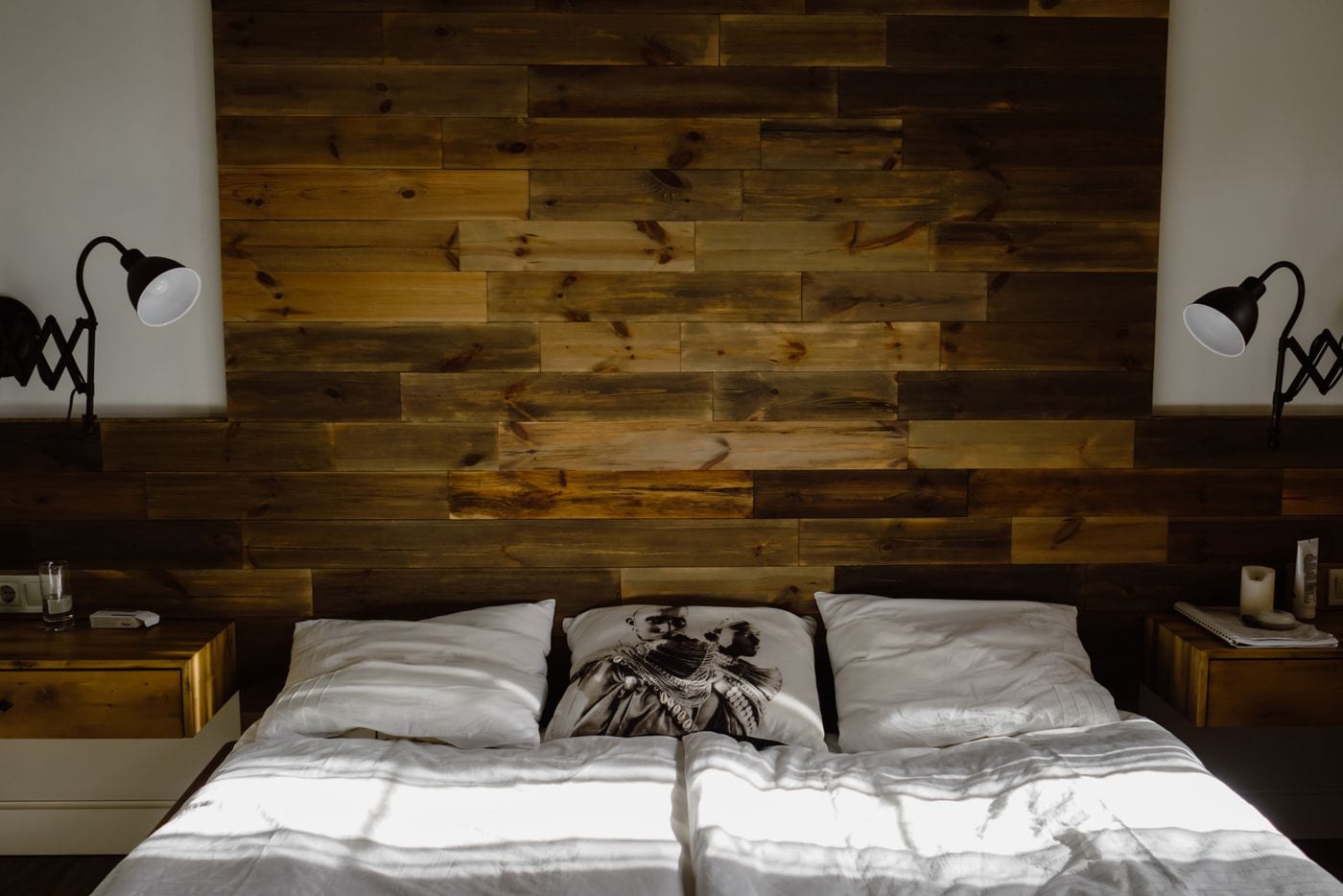 A bed with white linen against a warm solid-wood plank wall, framed by matching wood nightstands.