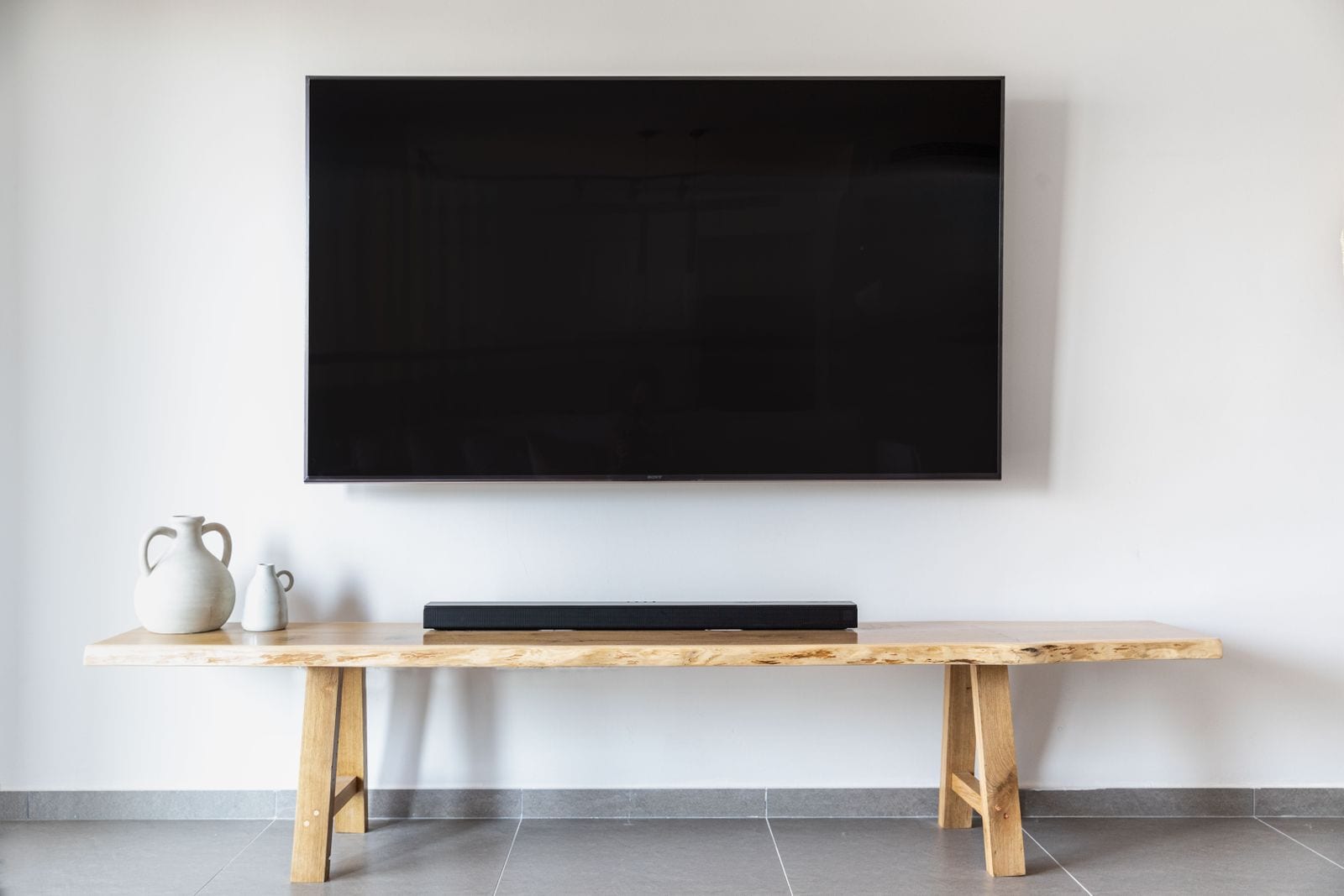 A flat-screen TV mounted flush and level on a plaster wall above a walnut console, cables hidden.